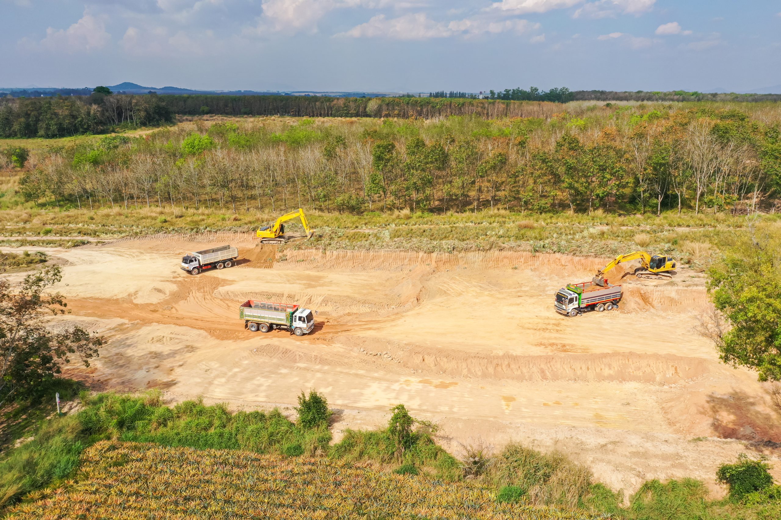 Aerial view of a land development site with excavators and dump trucks performing excavation and earthmoving work in a cleared construction area.